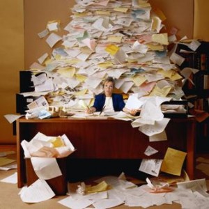 picture of a woman at her messy office desk piled high with papers